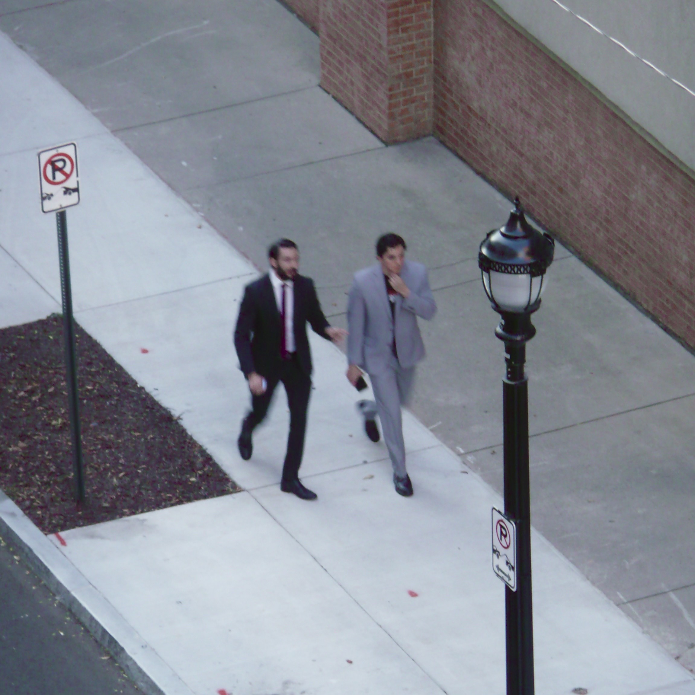 Two men in suits blurred in motion walking down a sidewalk. shot at a downward angle